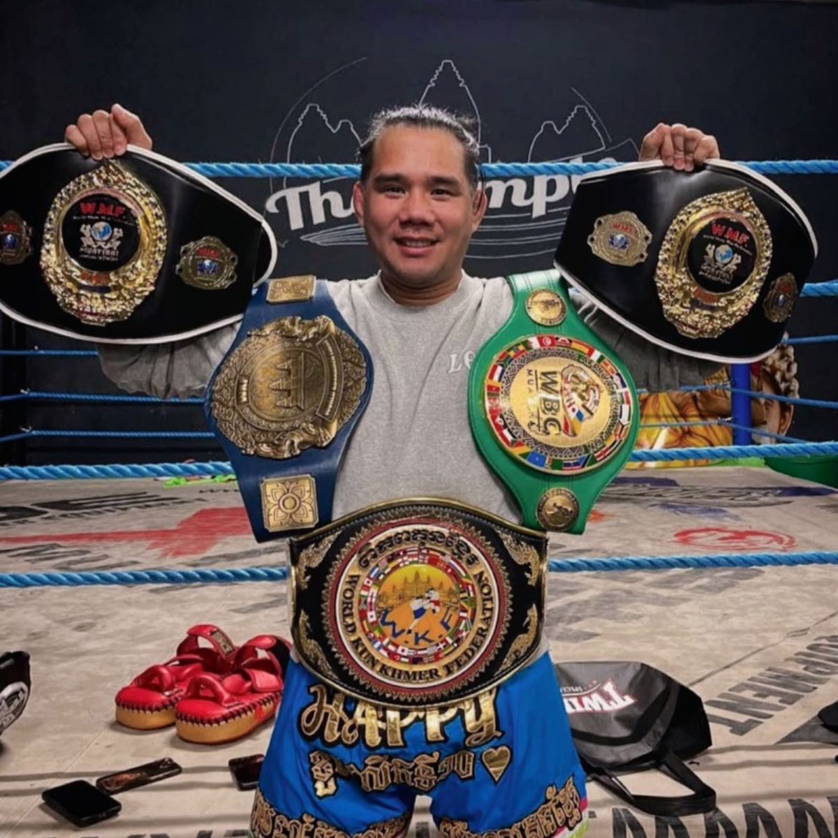Albert Veera Chey in the training ring holding his championship belts.