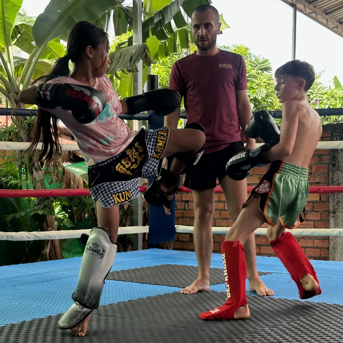 Two children sparring in the ring while Kevin supervises.