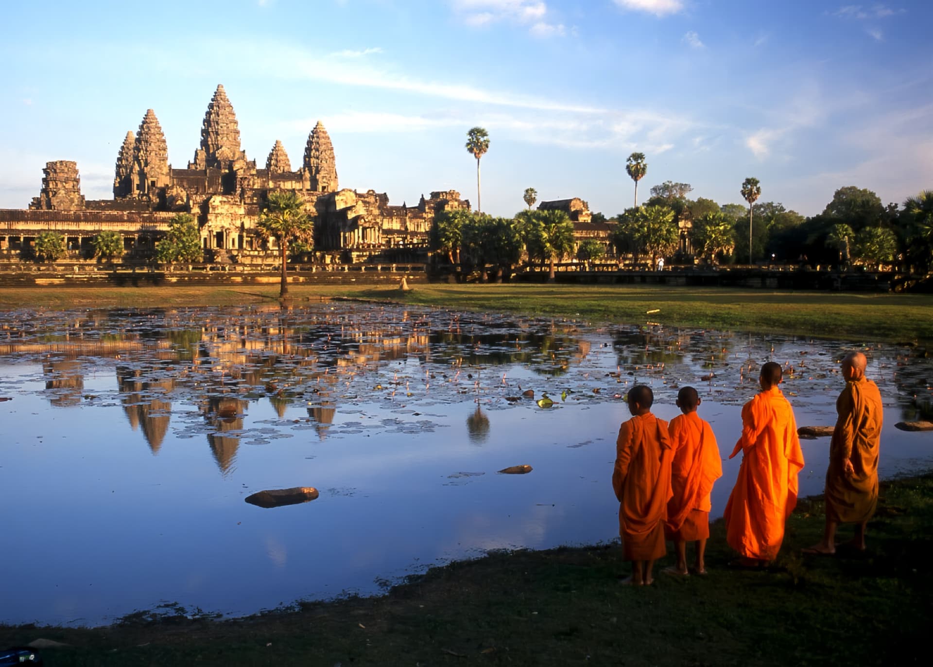 Angkor Wat reflected across the water, with Buddhist monks in the foreground.